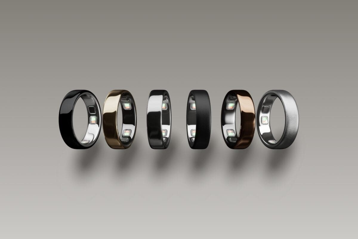 Six Oura Ring 5 smart rings in different colors, including black, gold, silver, and rose gold finishes, arranged in a row against a gray background.