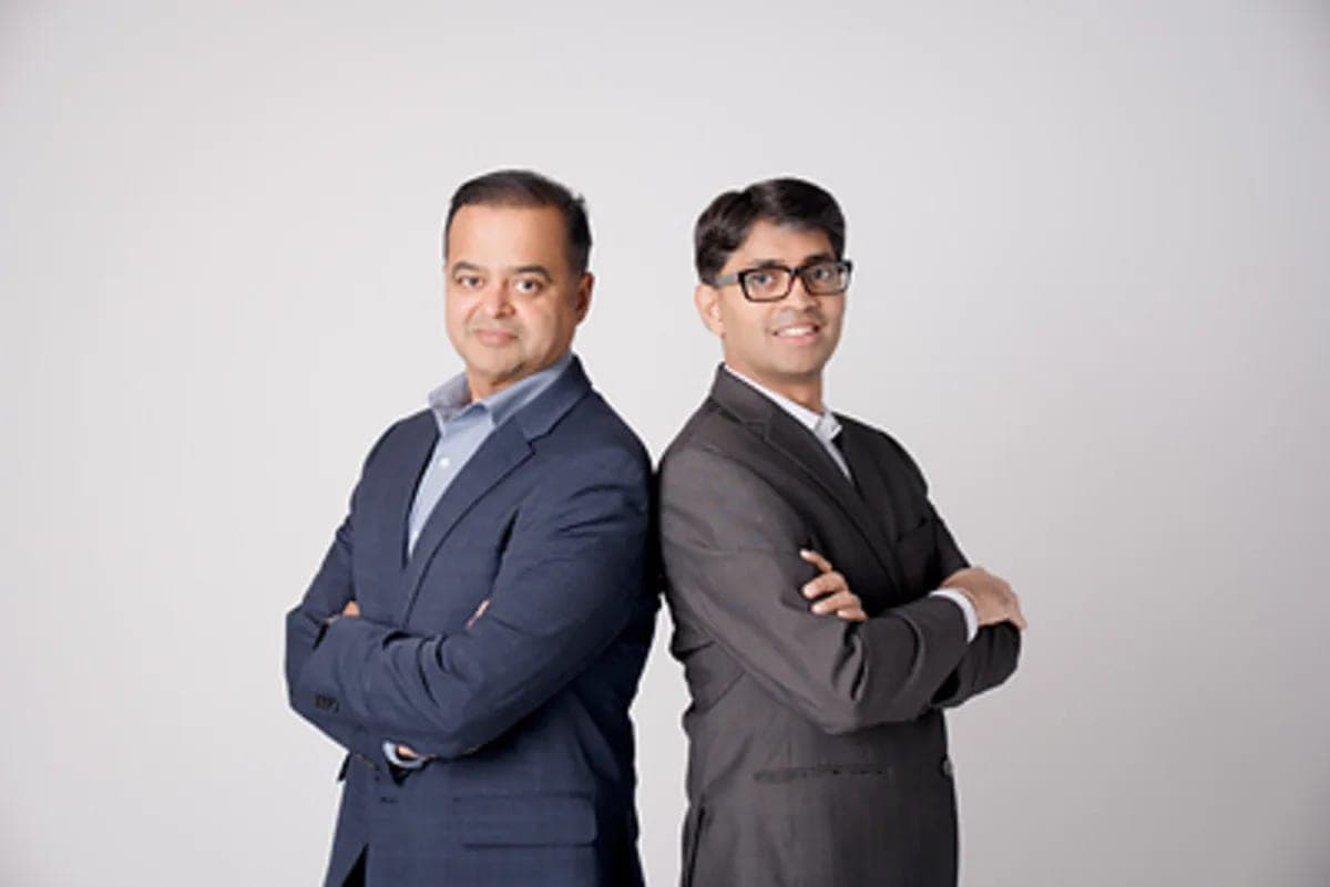 Two men in business suits standing back to back with arms crossed, smiling for a portrait