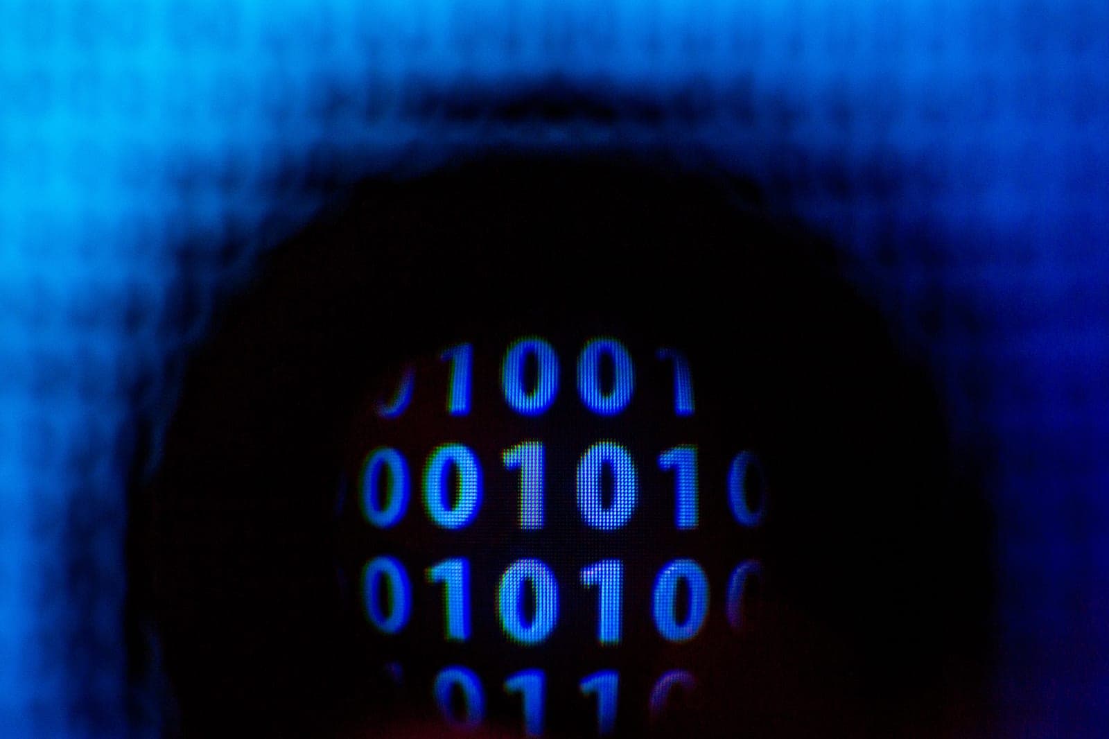 A blurred close-up of glowing blue binary digits, ones and zeros, on a dark screen
