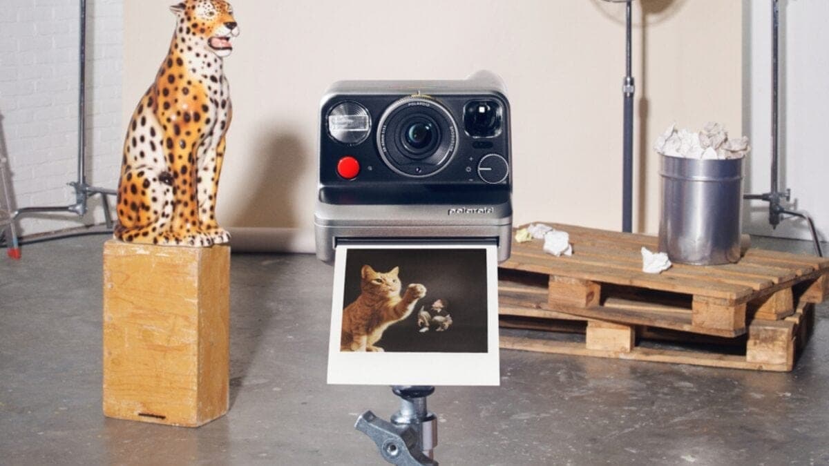 The Polaroid Mod instant camera on a stand next to a leopard figurine, printing out a photo of a cat, in a studio setting.