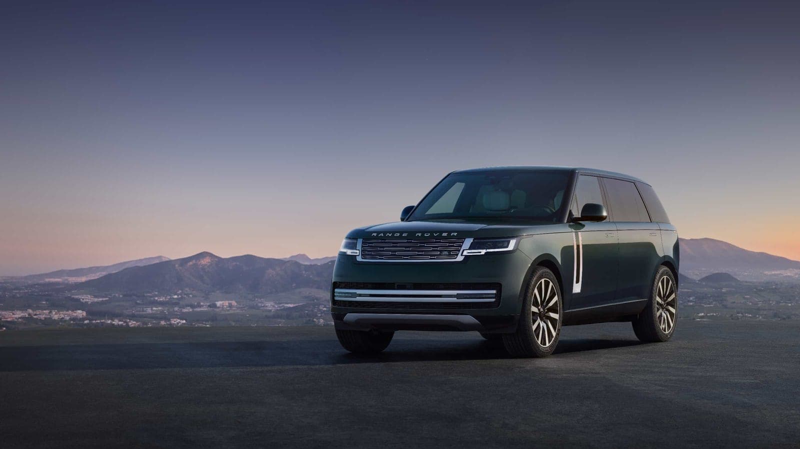 A dark green Range Rover Electric SUV parked on a hilltop overlooking mountains at dusk