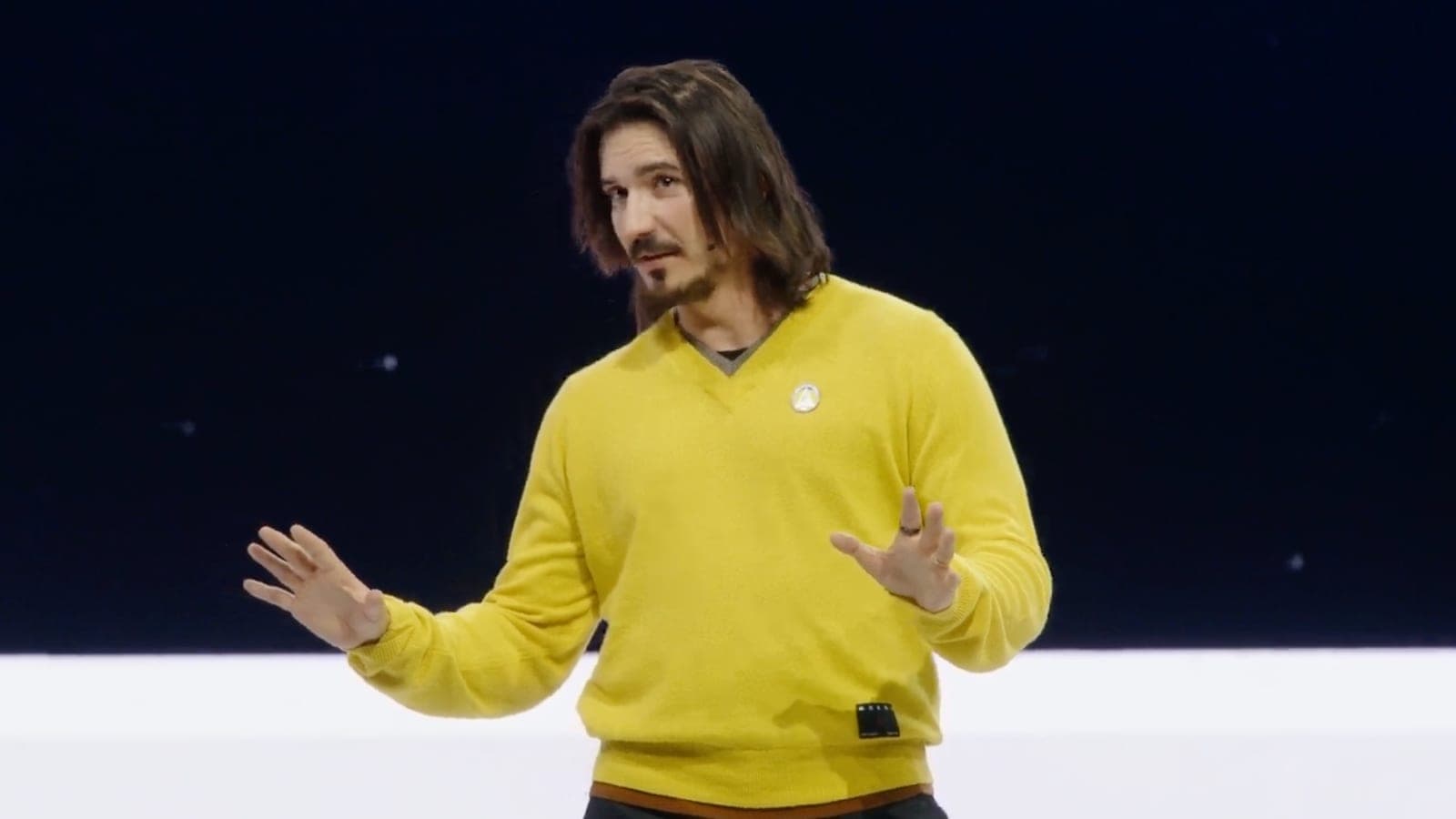 A presenter in a yellow sweater speaking on stage at Robinhood's HOOD Summit event