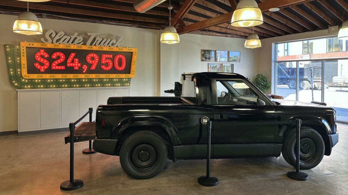 A black prototype Slate Truck parked in the Chicago showroom beside a marquee-style sign showing the $24,950 price