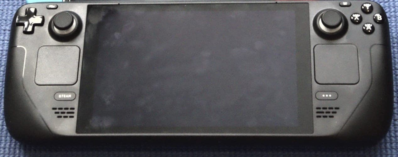 A black Steam Deck handheld gaming PC lying on a blue fabric surface, its screen turned off