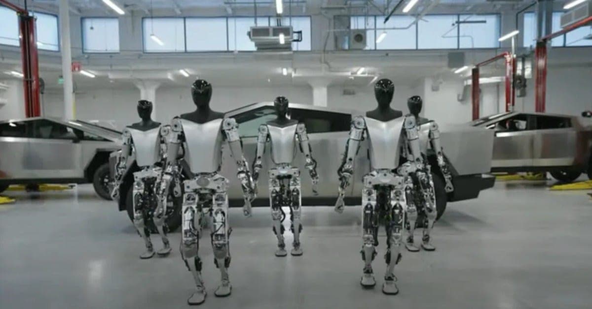 Several Tesla Optimus humanoid robots standing in a row in front of Cybertrucks inside a factory