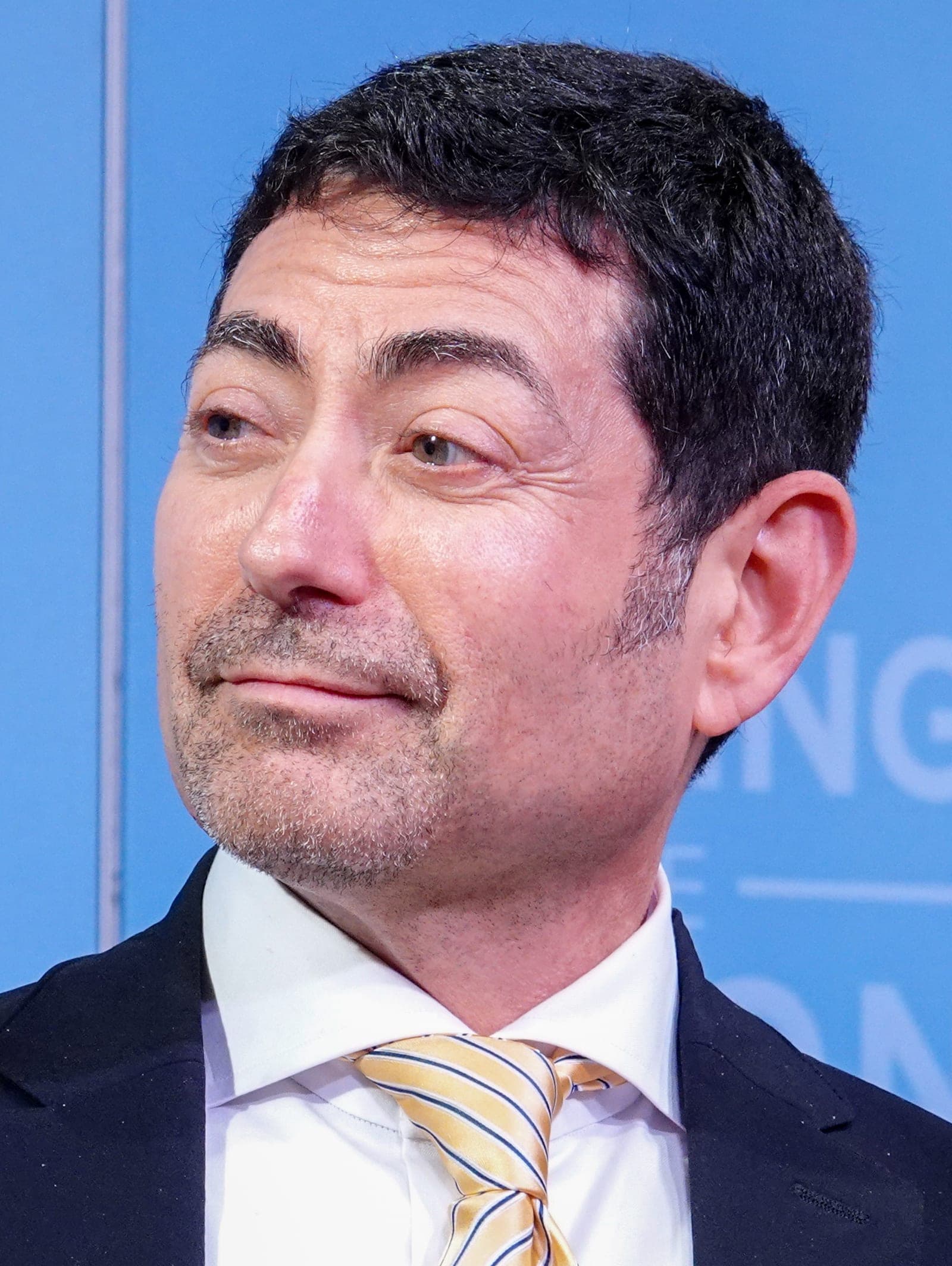 Close-up portrait of Mariano-Florentino Cuéllar wearing a suit and striped tie at a public event
