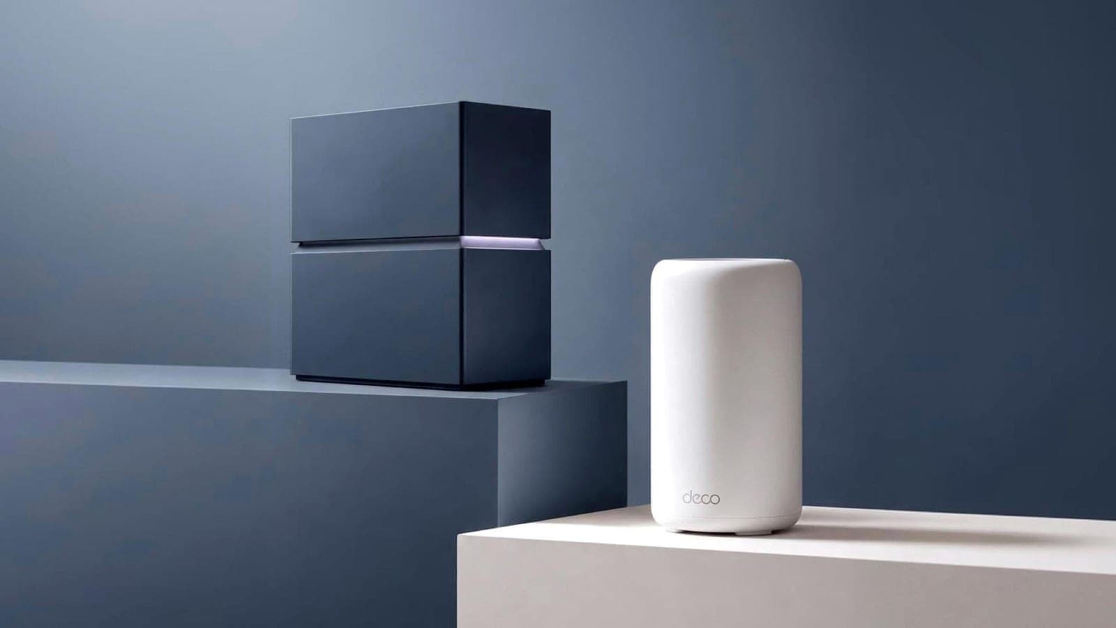 Two TP-Link Deco mesh Wi-Fi units on pale pedestals, a dark square one and a white cylinder, against a blue-gray backdrop