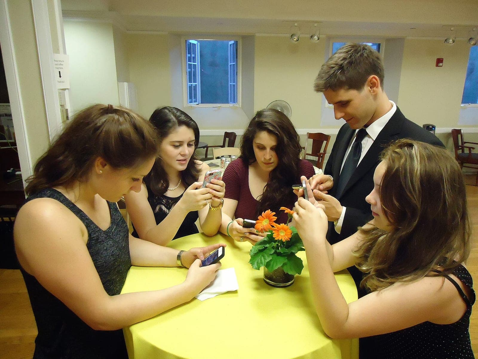 A group of young people standing around a table looking at their smartphones