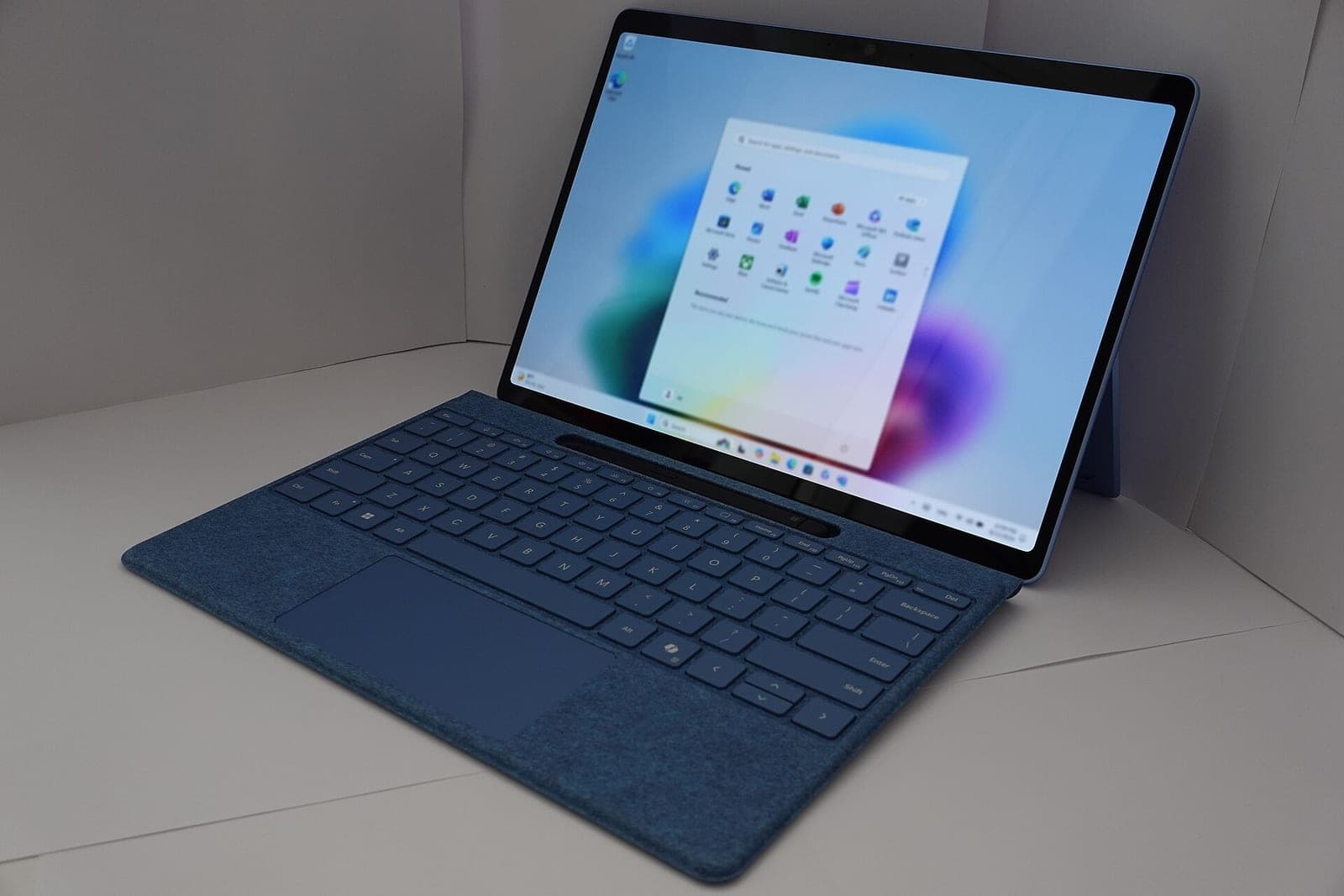 A Microsoft Surface Pro laptop with a blue keyboard cover, showing the Windows 11 Start menu on its screen